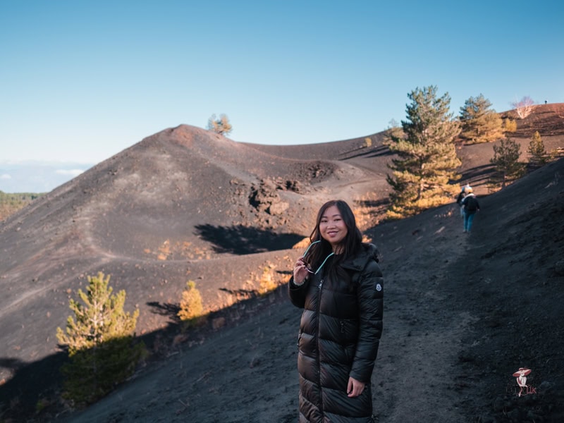 Exclusive trips to Mount Etna from catania: Elegant and Stress-free Options 20 Janey hiking on a live volcano at 2000 metres above sea level, with spectacular views of the craters, wearing a black puffer jacket.