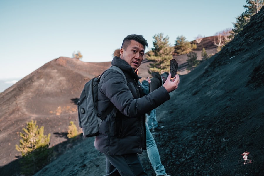 Exclusive trips to Mount Etna from catania: Elegant and Stress-free Options 26 A traveller holding up a small piece of black volcanic rock as he hiked on Mt Enta with a local guide explaining where they came from.